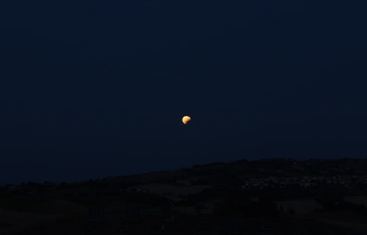 Luna piccina in mezzo al cielo sopra una collina